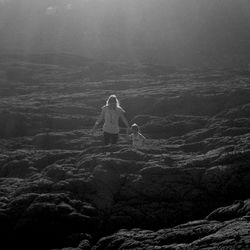Rear view of woman standing on rock by sea