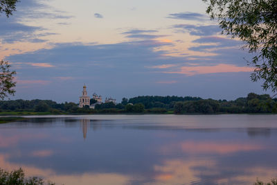 Scenic view of lake by buildings against sky during sunset