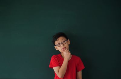 Thoughtful boy looking away while standing against blackboard in classroom