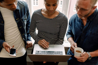 High angle view of businesswoman holding laptop while discussing with colleagues in office