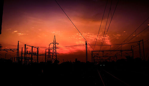 Silhouette electricity pylons against sky during sunset