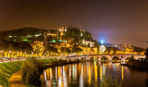 Illuminated bridge over river in city against sky at night