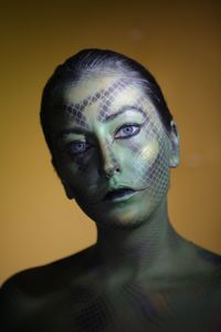 Portrait of young woman with face paint against colored background