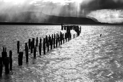 Silhouette wooden posts on beach against sky