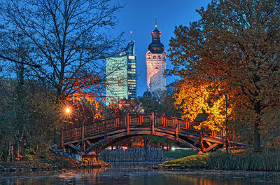 Illuminated bridge over river by buildings against sky