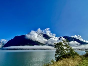 Scenic view of fjord against mountain covered in clouds with clear sky above