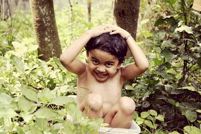 Portrait of cheerful wet shirtless boy sitting in yard