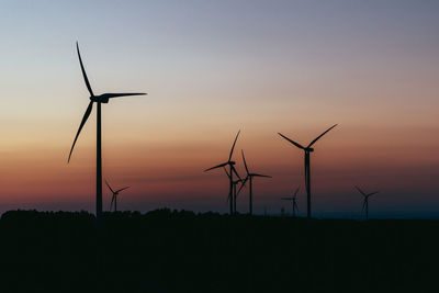 Silhouette wind turbines on field against sky during sunset