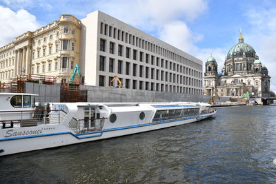 Boats in canal by buildings against sky in city