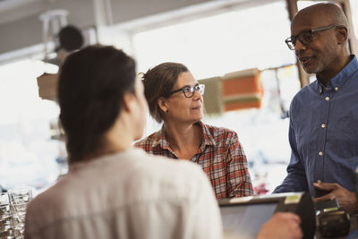 Women looking at senior male customer talking while standing by checkout counter in store