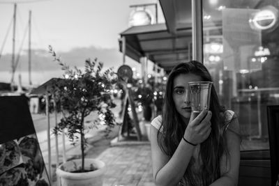 Portrait of young woman holding glass at outdoor restaurant