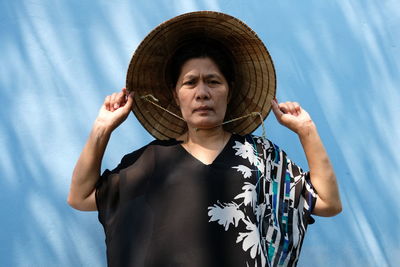 Mature woman wearing asian style conical hat against wall