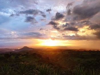 Scenic view of landscape against cloudy sky during sunset