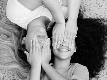 High angle view of smiling mother and daughter covering eyes while lying on floor