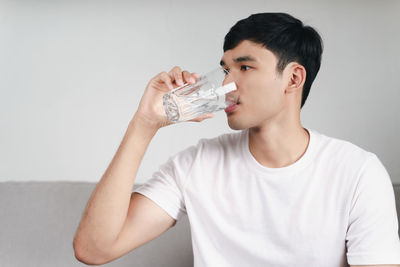 Portrait of young man drinking glass against white background