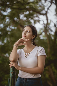 Young woman looking up while standing against trees