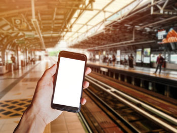 Low section of person holding smart phone on railroad tracks