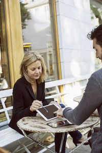 Business colleagues using digital tablet at sidewalk cafe