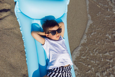 Child boy in sunglasses, a white t-shirt lies on an inflatable mattress on the seashore