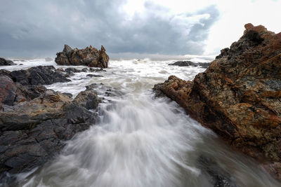 Long exposure image of waves crashing at beach against storm clouds