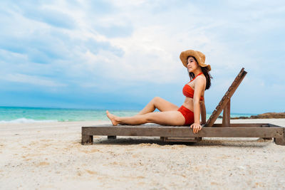 Woman sitting on beach against sky