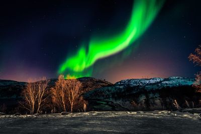 Aurora borealis over landscape against sky at night