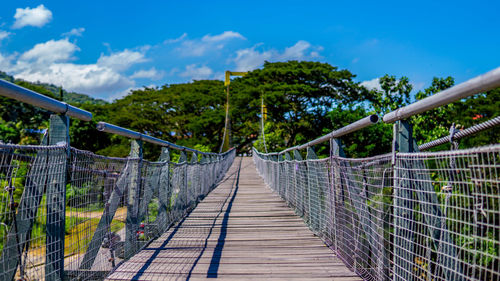 Footbridge amidst trees against sky