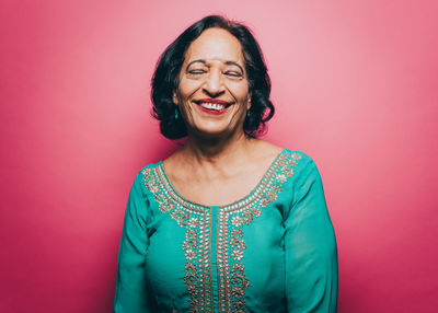 Smiling senior woman with eyes closed over pink background