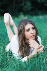 Thoughtful young woman lying on grassy field