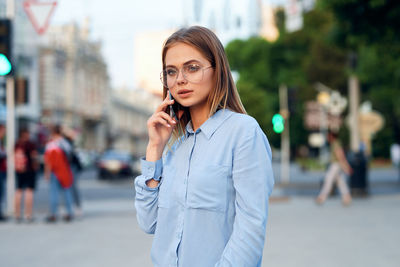 Portrait of young woman talking on mobile phone while standing in city