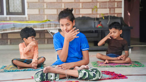 Group of children engaged in yoga at home sitting on the mat.