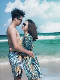 Young couple standing at beach against sky