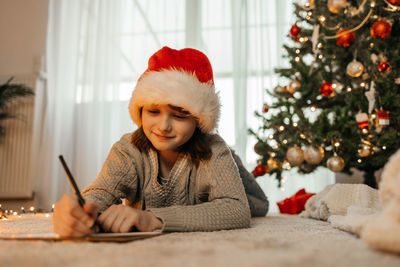 New year's and christmas. a teenage girl in a santa claus hat writes a letter to santa claus 