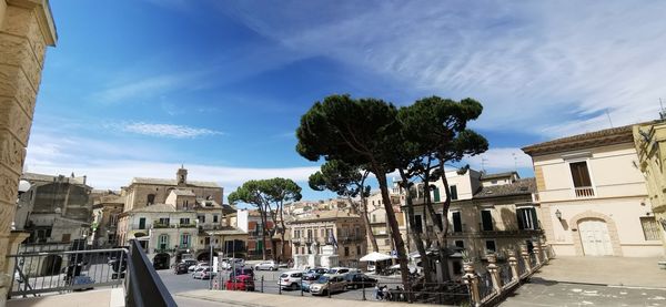 Trees by buildings against sky in city