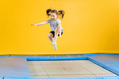 Full length of woman jumping against yellow wall