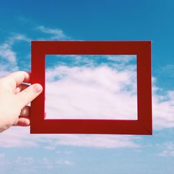 Hand holding red frame against sky