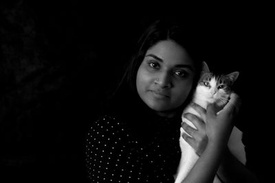 Portrait of woman holding cat against black background