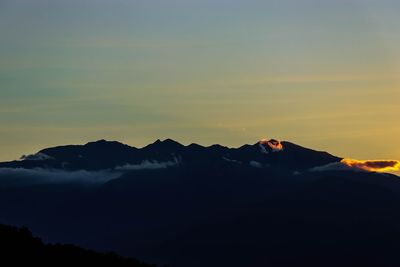 Silhouette man relaxing on mountain against sky during sunset