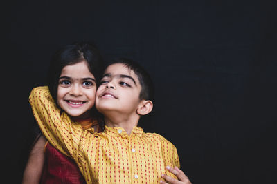 Smiling siblings against black background