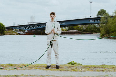 Full length portrait of confident man holding garden hose near river