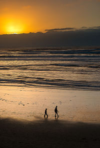 Silhouette people on beach against sky during sunset