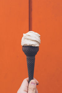 Human hand holding ice cream cone against orange wall