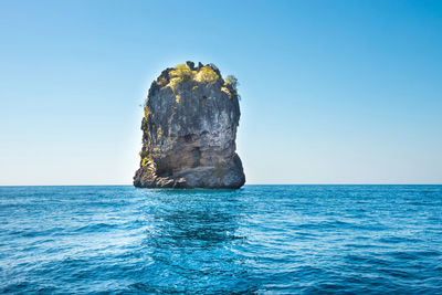 Rock formation in sea against clear blue sky