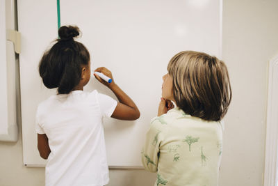 Boy looking at schoolgirl writing on whiteboard in elementary school