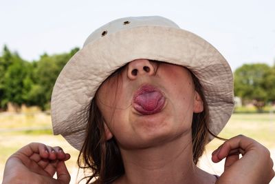 Close-up of woman wearing hat while sticking out tongue outdoors