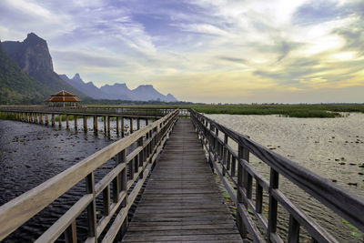 Wooden boardwalk leading towards water against sky