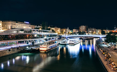 Illuminated buildings by river against sky at night