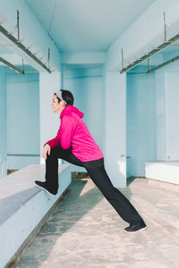 Side view of woman stretching on railing against blue wall