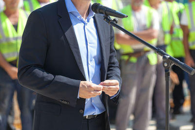 Midsection of man giving speech while workers standing in background