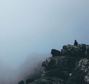 Rear view of woman sitting on cliff against sky